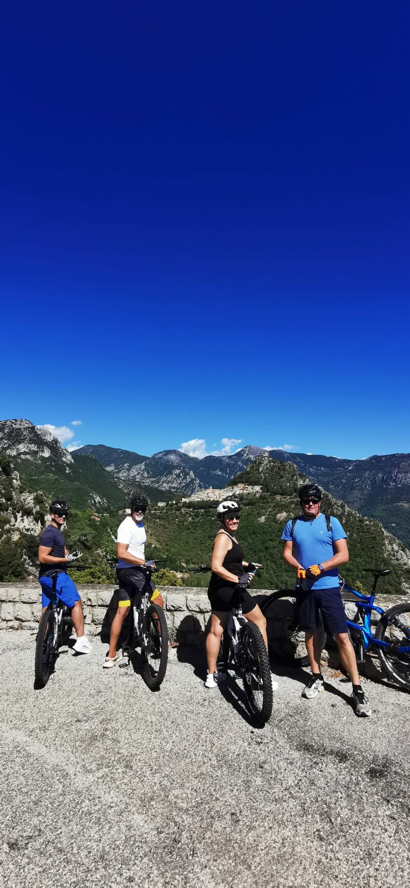 Quatre cyclistes souriants posent avec leurs VTT, un village perché en arrière-plan