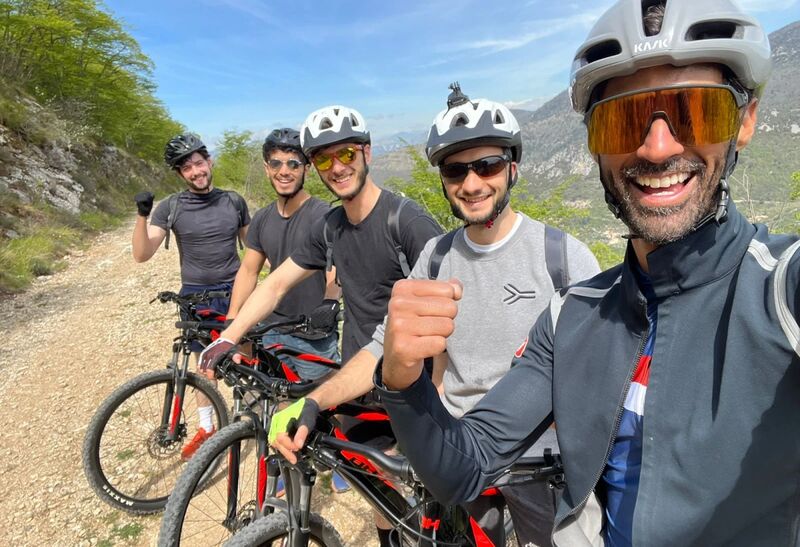 Cinq cyclistes casqués et souriants posent avec leurs VTT électriques sur un sentier de montagne