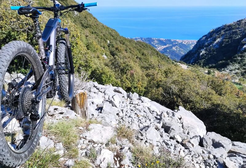 Un VTT électrique arrêté sur un éboulis calcaire, avec la Méditerranée et la côte en contrebas