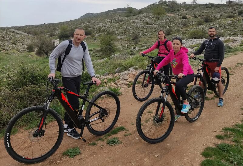 Quatre cyclistes en VTT électrique sur une piste caillouteuse traversant un plateau de garrigue